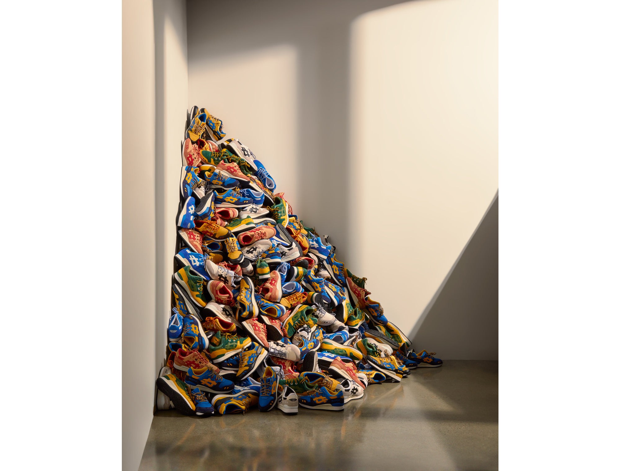 A mound of multihued sneakers in the corner of a vacant room.