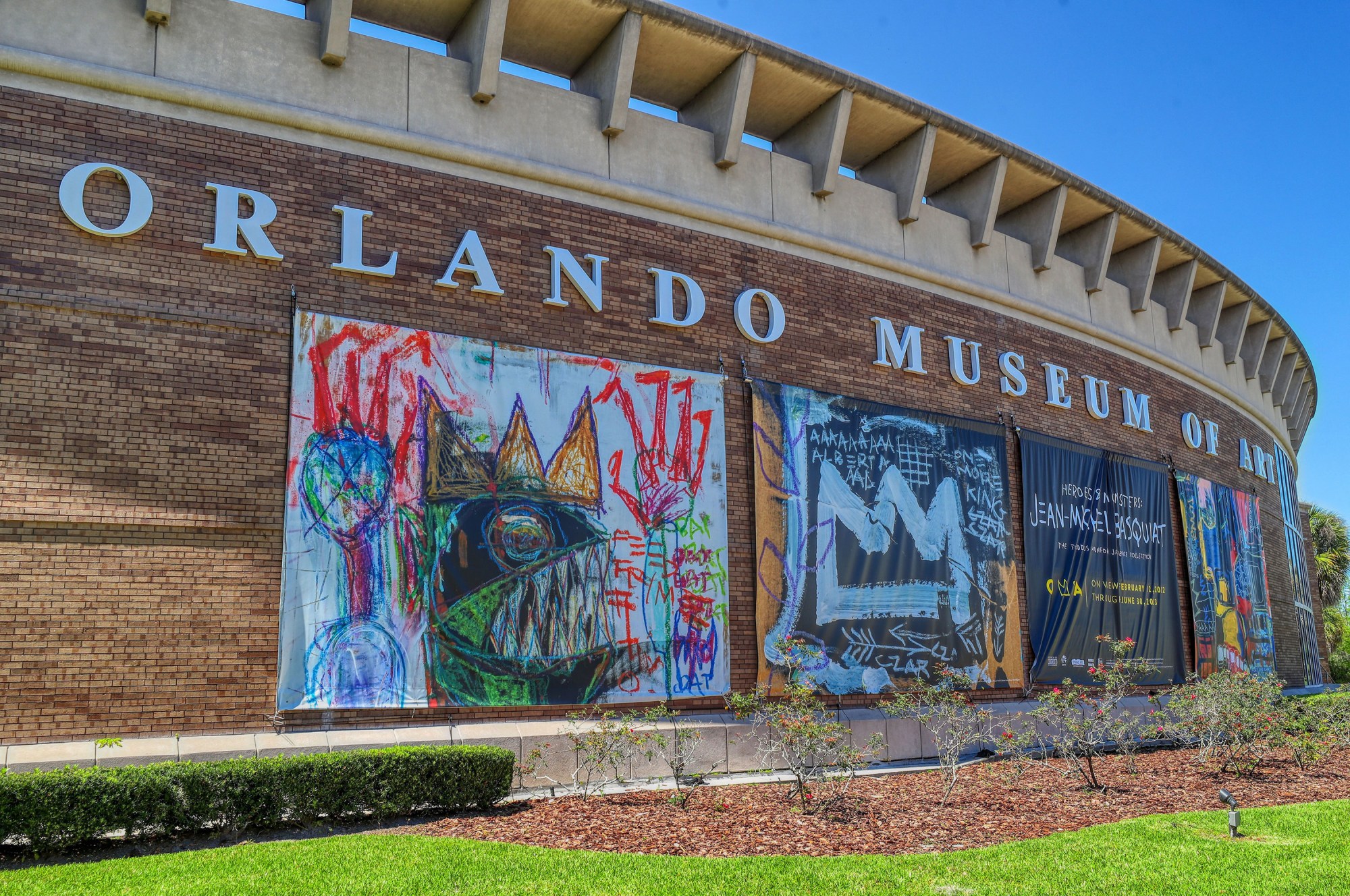 Brushy Basquiat-style paintings adorn banners on a low, cylindrical brick building that bears the words "Orlando Museum of Art."